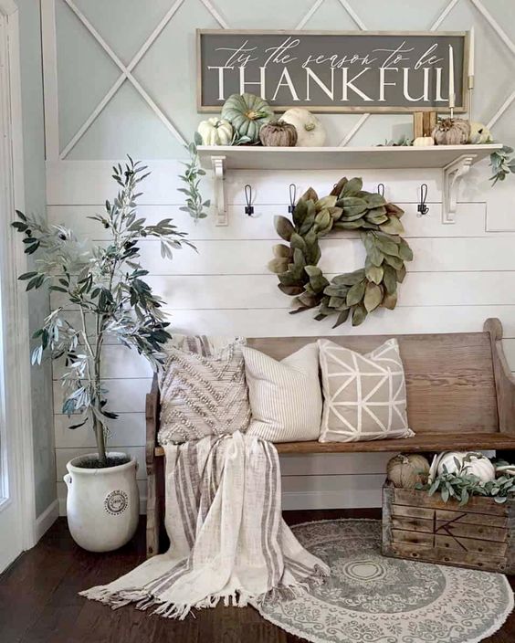 a neutral farmhouse entryway with a leaf wreath, a potted tree, faux pumpkins, candles and neutral textiles
