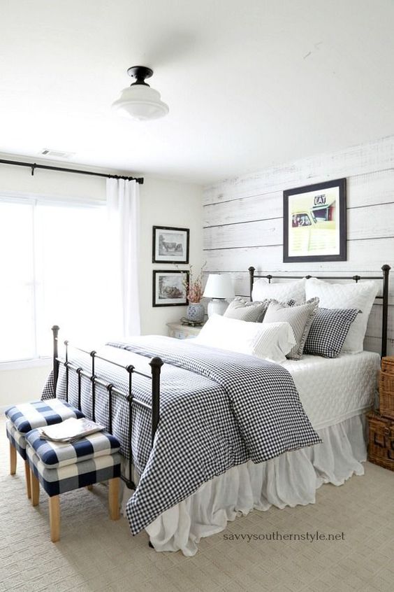 a neutral farmhouse space with a whitewashed wall, a forged bed, buffalo check stools and artworks