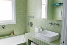 a pretty laconic modern bathroom clad with light green small scale tiles, with a vanity clad with tiles, a mirror cabinet and a white storage unit