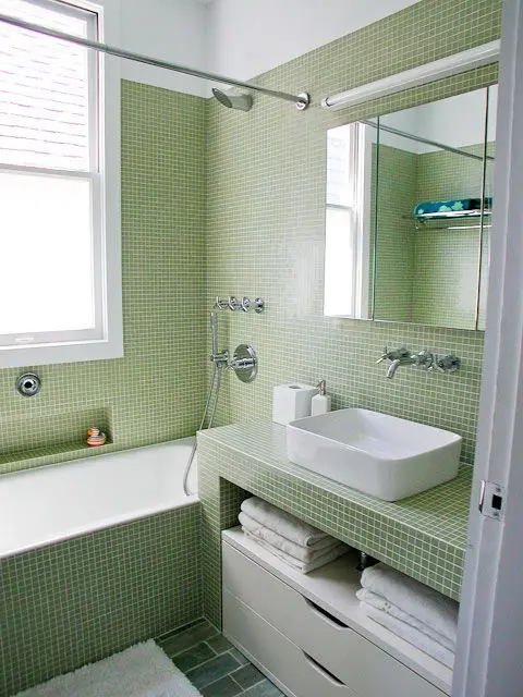 a pretty laconic modern bathroom clad with light green small scale tiles, with a vanity clad with tiles, a mirror cabinet and a white storage unit