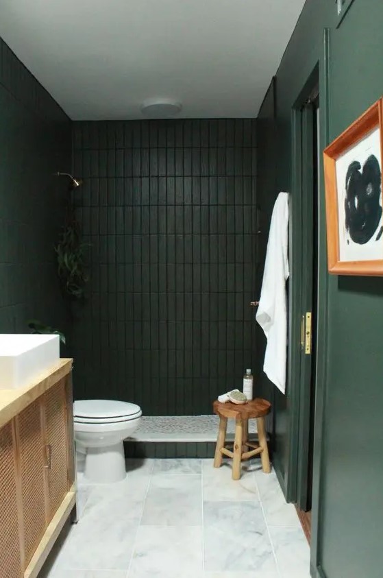 a refined and moody dark green and black bathroom with a white marble tile floor and a wooden vanity