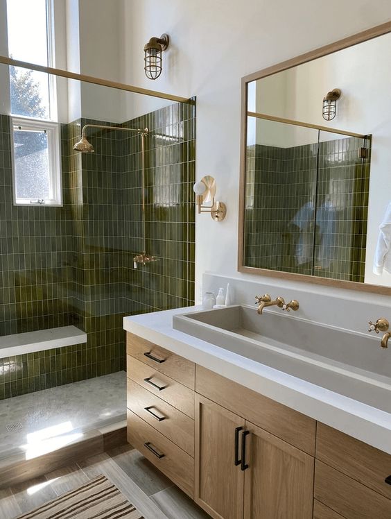 a refined bathroom with dark green skinny tiles in the shower, a stained vanity, a large mirror and gold appliances