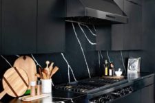a refined black kitchen with metal cabinets, a marble backsplash and countertops and a black hood