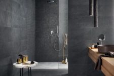 a refined graphite grey bathroom clad with various tiles, with pendant lamps, a wooden vanity and a marble mini table