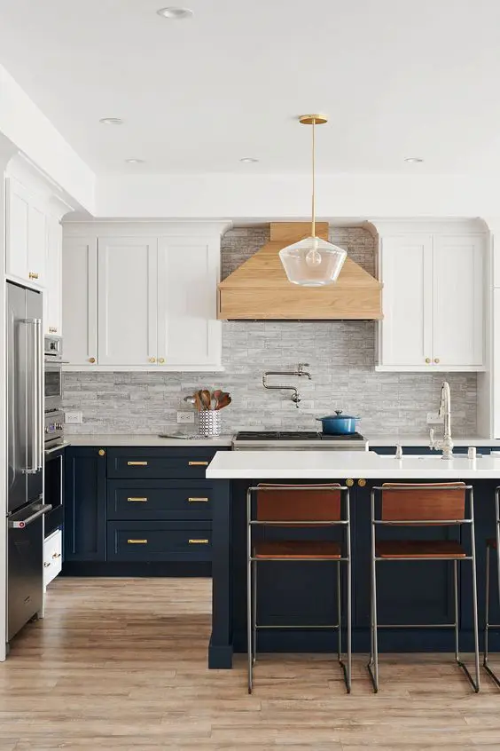 A refined two tone kitchen with white and navy shaker cabinets, a grey tile backsplash, leather chairs and a pendant lamp