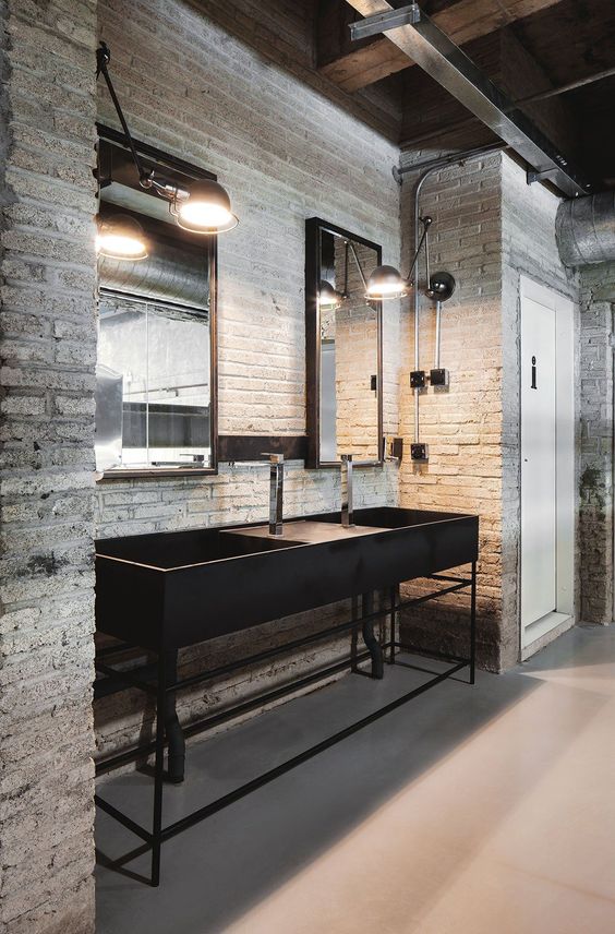 a rough industrial bathroom clad with white bricks, a black stone vanity and black vintage lamps and mirrors