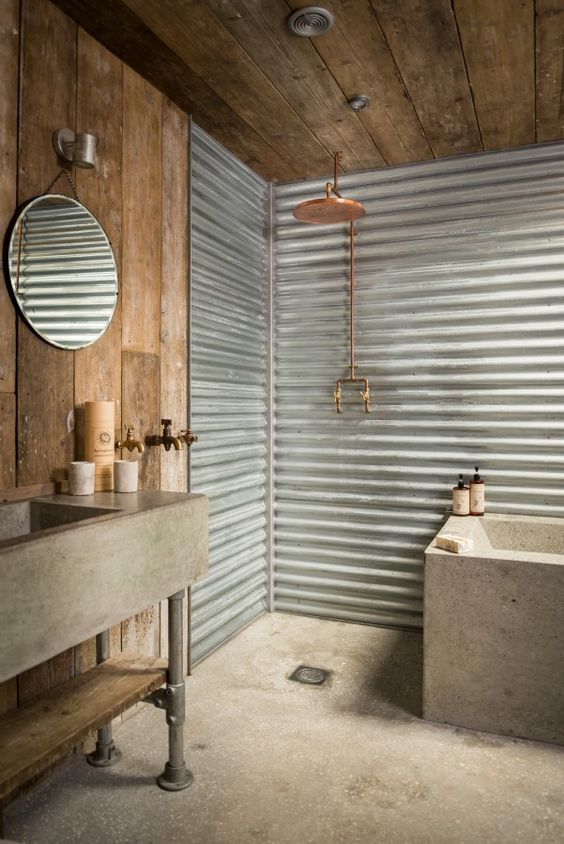 a rustic industrial bathroom with a reclaimed wooden ceiling and wall, corrugated steel walls, a concrete bathtub and sink on metal legs