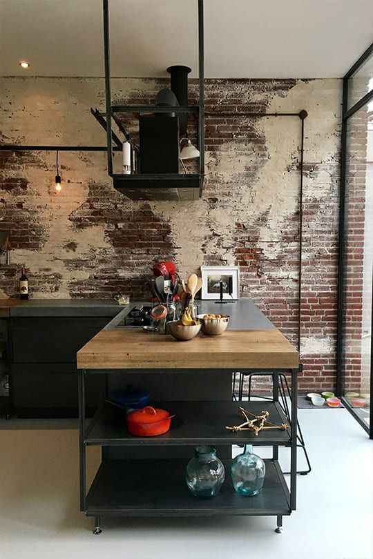 a shabby industrial kitchen with rusty brick walls, black metal cabinets and kitchen island and exposed pipes