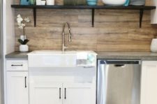 a simple farmhouse kitchen in white with a wooden backsplash and dark open shelving looks catchy and cozy