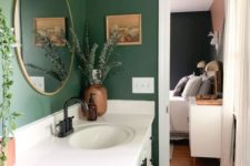 a small bathroom with hunter green walls, a white vanity, printed textiles and greenery in vases and pots