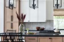 a sophisticated two-tone kitchen with white and stained cabinets, black countertops, mosaic tiles and black pendant lamps