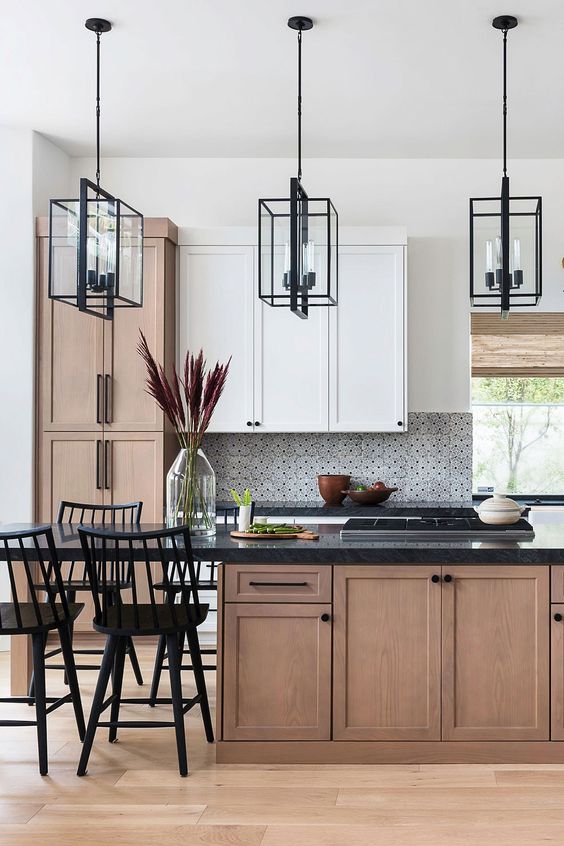 A sophisticated two tone kitchen with white and stained cabinets, black countertops, mosaic tiles and black pendant lamps