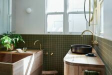 a spa-style bathroom clad with green square tiles, with a wooden ofuro tub and a wooden vanity, a black sink and gold fixtures