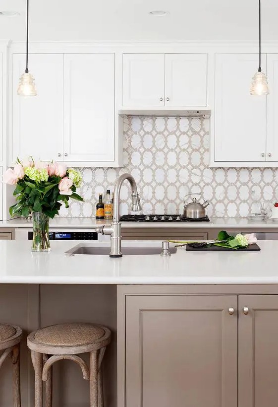 a stylish and elegant kitchen with taupe lower cabinets and white upper ones, a pretty tile backsplash, wooden stools, pendant lamps and elegant vintage fixtures