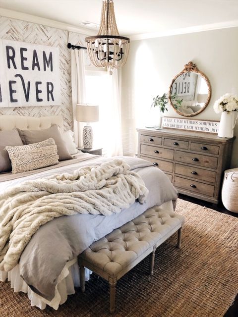 a stylish farmhouse bedroom with neutral walls, rustic vintage furniture, a vintage chandelier and a refined mirror