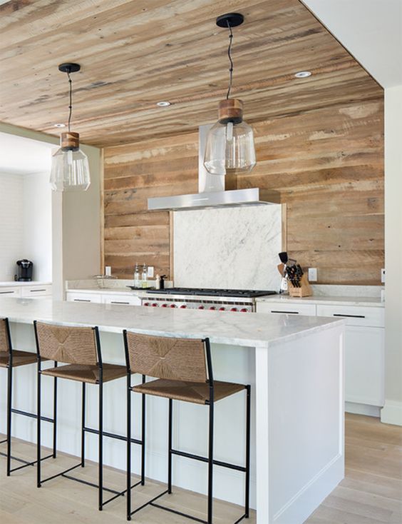 a stylish farmhouse kitchen with white lower cabinets, a marble backsplash and kitchen island, a wooden wall that goes up to the ceiling