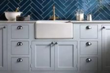 a stylish kitchen with dove grey cabinets, a navy herringbone tile backsplash, an open shelf, printed tiles on the floor