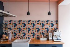 a stylish kitchen with navy cabinets, blush walls, a coral ceiling and a bright printed tile backsplash