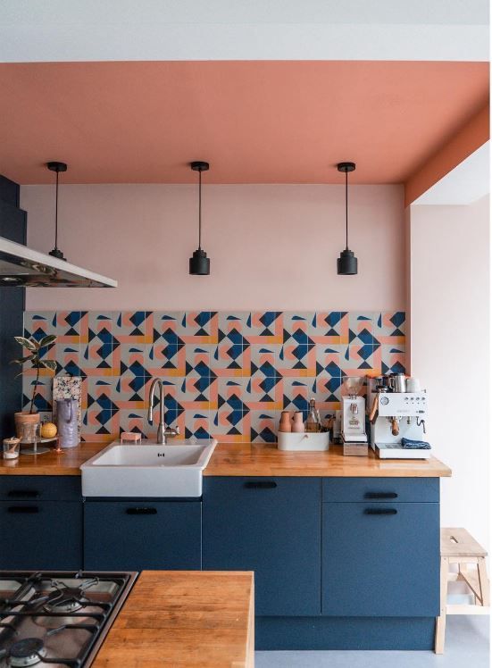 a stylish kitchen with navy cabinets, blush walls, a coral ceiling and a bright printed tile backsplash