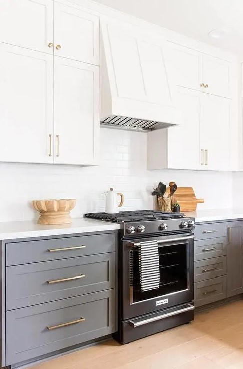 a stylish kitchen with white upper cabinets and grey lower ones, a white subway tile backsplash and white countertops plus gold handles