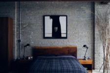 a stylish masculine industrial bedroom with brick walls, stained wooden furniture, plaid bedding and metal table lamps