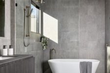 a stylish minimalist bathroom in grey, clad with tiles, with a floatign vanity and a free-standing bathtub