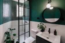 a stylish modern bathroom with green and white walls, with penny tiles in the shower, a black vanity and a round mirror