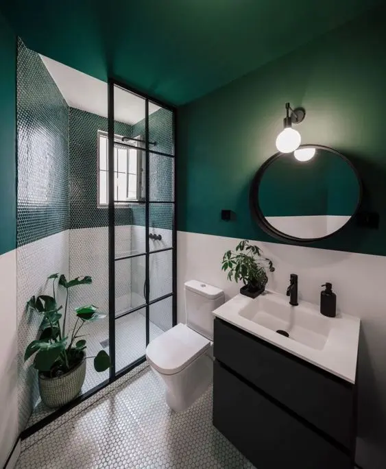 a stylish modern bathroom with green and white walls, with penny tiles in the shower, a black vanity and a round mirror
