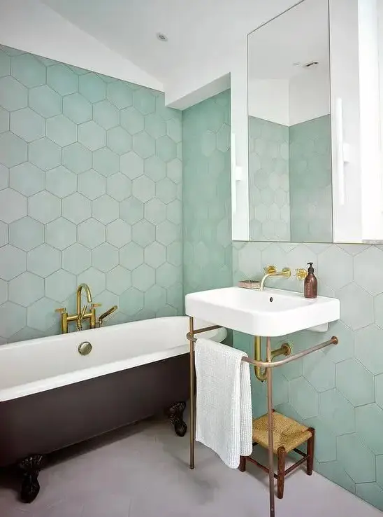 a stylish modern bathroom with green hexagon tiles, a black clawfoot tub, a white free standing sink and a woven stool
