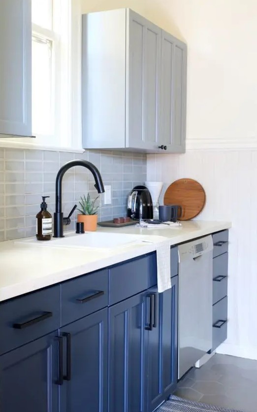 a stylish small kitchen with dove grey and bold blue cabinets, a grey tile backsplash, a white stone countertop