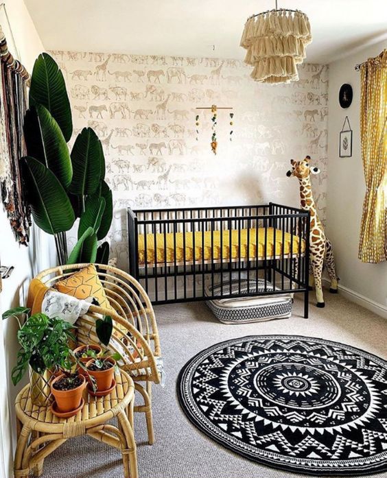 a super bold safari nursery with an animal print wall, a black crib with mustard bedding, a tassel chandelier, rattan furniture and potted plants plus a printed rug