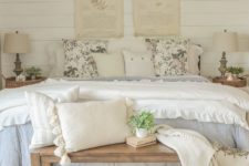 a sweet and chic farmhouse bedroom with pretty bedding, a wooden bench, baskets and vintage posters on the wall