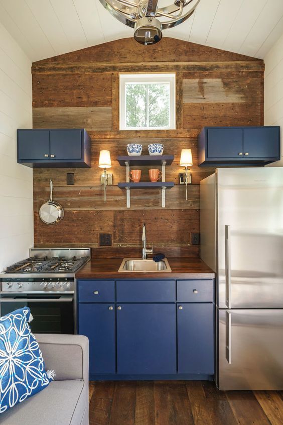 a tiny yet chic kkitchen with navy cabinets and a wooden backsplash wall plus a matching countertop is really cool