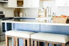 a tow-tone kitchen with white upper and blue lower cabinets, white countertops, white upholstered stools and pendant lamps