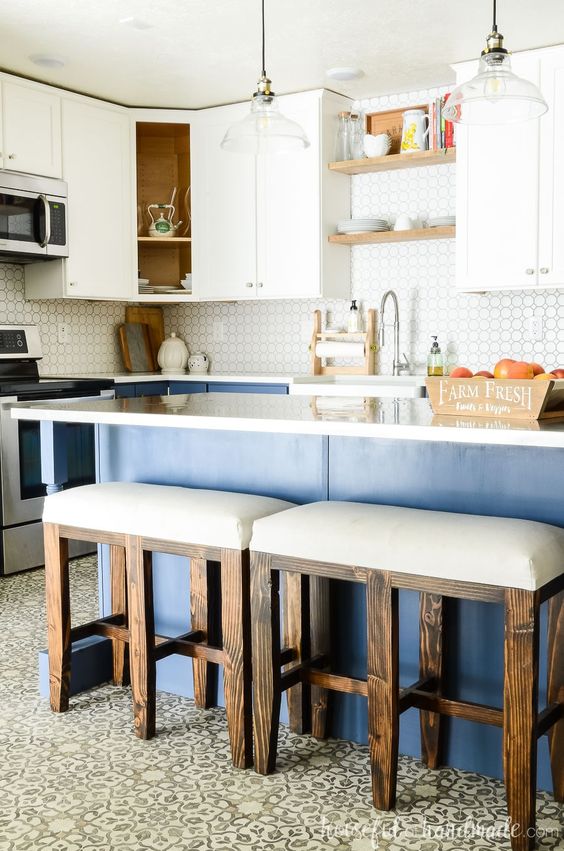 A tow tone kitchen with white upper and blue lower cabinets, white countertops, white upholstered stools and pendant lamps