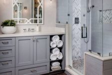 a traditional grey bathroom done with various tiles, a grey vanity with much storage space potted greenery and lots of lights