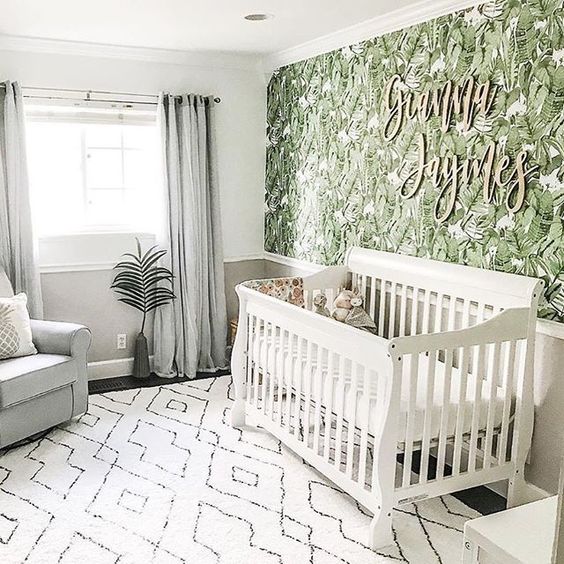 a tropical nursery with a tropical leaf wall, neutral furniture, a printed rug and some greenery