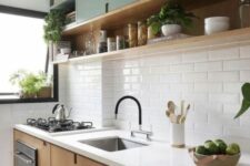 a two-tone kitchen with green and stained cabinets, white subway tiles and a shelf, potted plants and black fixtures