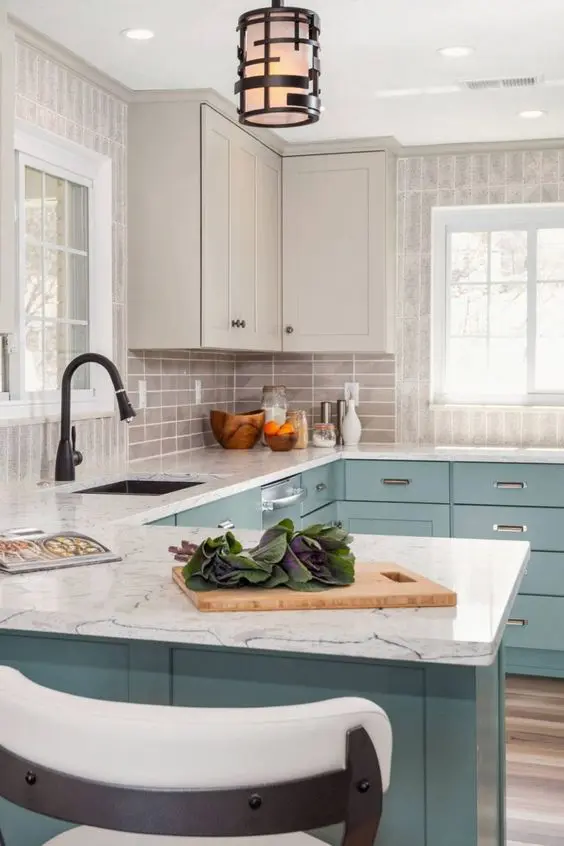 A two tone kitchen with light grey and blue cabinets, a grey tile kitchen backsplash and white stone countertops