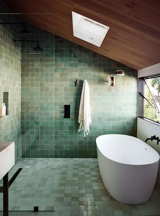 a very peaceful green tile bathroom with a wooden ceiling and a skylight, an oval tub and black fixtures