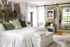 a vintage farmhouse bedroom with brick walls, reclaimed wood, shabby shutters, greenery and green pillows plus vintage chandeliers