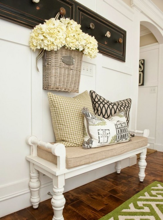a vintage farmhouse entryway with racks with knobs, a vintage white bench with a burlap cushion and a rug