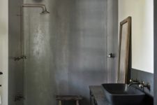 a vintage industrial bathroom with shower walls of concrete, a black vanity and a black sink plus vintage fixtures