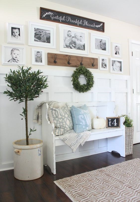 a welcoming farmhouse entryway with a gallery wall of family pics, a white bench with pillows, potted plants and a rack