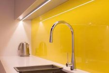 a white sleek kitchen with white countertops and a bold yellow glass backsplash that creates a mood and adds a sunny feel to the space