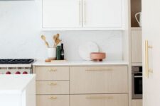 an airy kitchen with white and stained cabinets, white stone countertops and a backsplash, gold handles