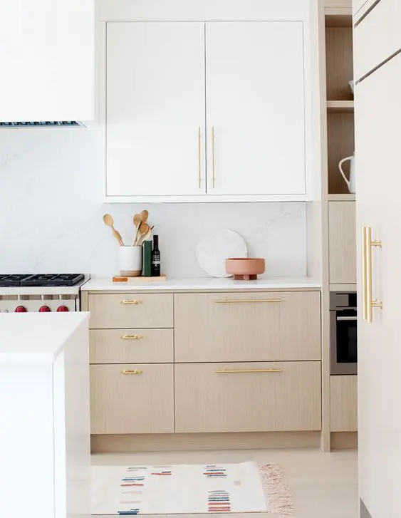 an airy kitchen with white and stained cabinets, white stone countertops and a backsplash, gold handles