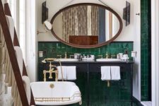 an art deco bathroom clad with emerald tiles, a green tub, a grey vanity and a large mirror in a copper frame