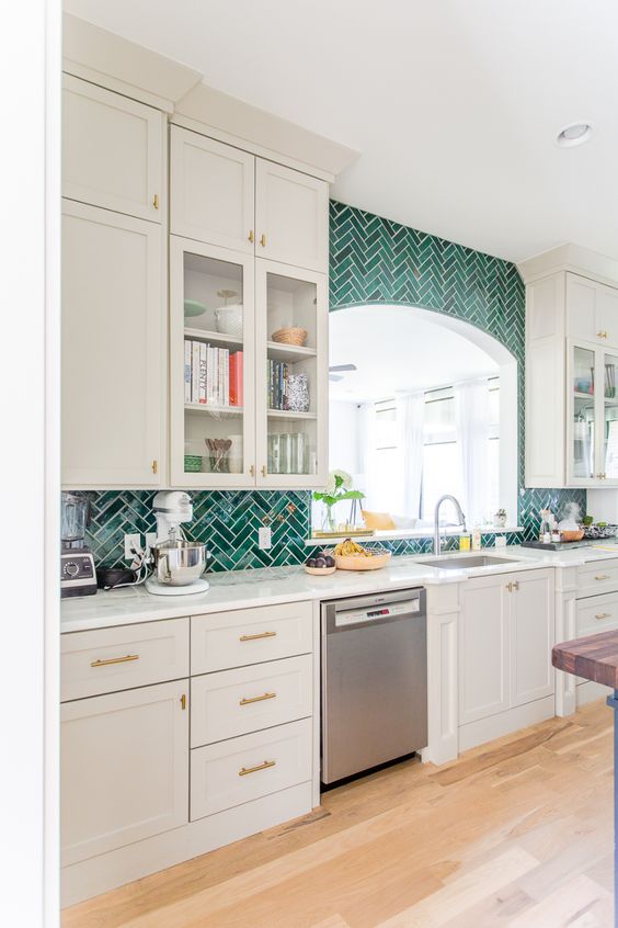 an elegant white kitchen with farmhouse cabinets, a bold emerald herringbone tile backsplash and white countertops