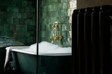 an exquisite dark green clawfoot bathtub surrounded with glossy green tiles on the walls